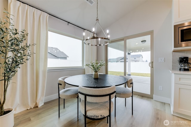 dining room featuring light wood finished floors, baseboards, and vaulted ceiling