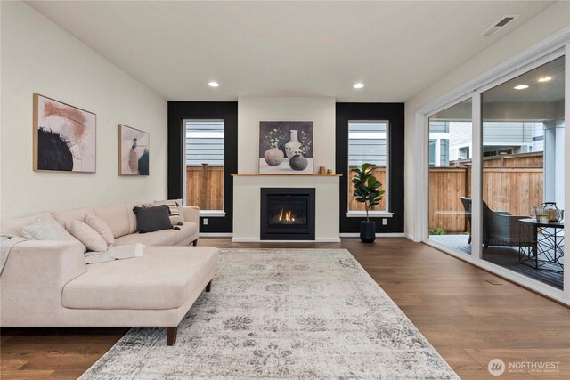 living area featuring visible vents, recessed lighting, dark wood-type flooring, and a glass covered fireplace