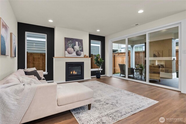 living area with a glass covered fireplace, recessed lighting, wood finished floors, and visible vents