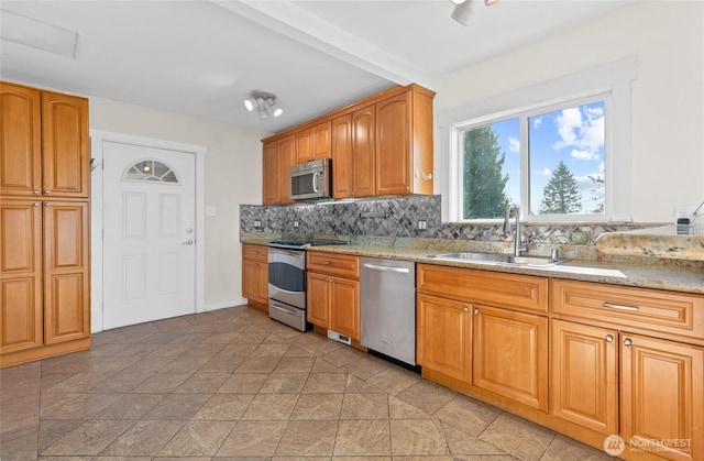 kitchen featuring decorative backsplash, brown cabinets, light stone countertops, stainless steel appliances, and a sink