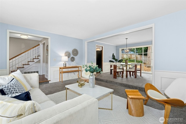 carpeted living room featuring stairs, a notable chandelier, and wainscoting