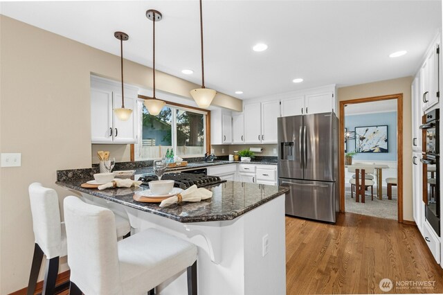 kitchen featuring dark stone countertops, a peninsula, stainless steel appliances, white cabinetry, and decorative light fixtures