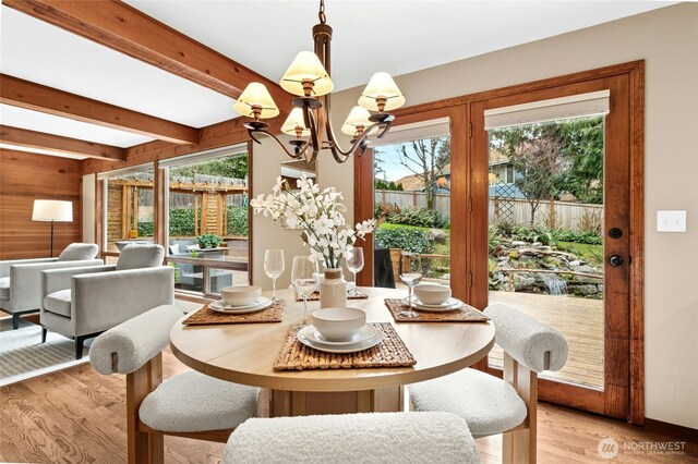 dining room featuring baseboards, beamed ceiling, wood walls, light wood-type flooring, and an inviting chandelier