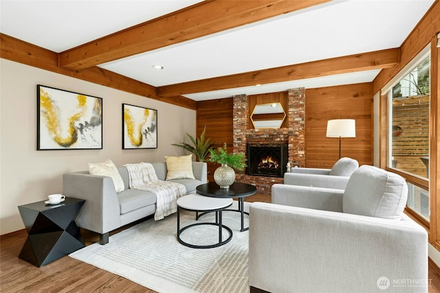 living area featuring a brick fireplace, wood finished floors, beam ceiling, and wood walls