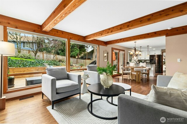 living area with visible vents, beamed ceiling, light wood-type flooring, and an inviting chandelier