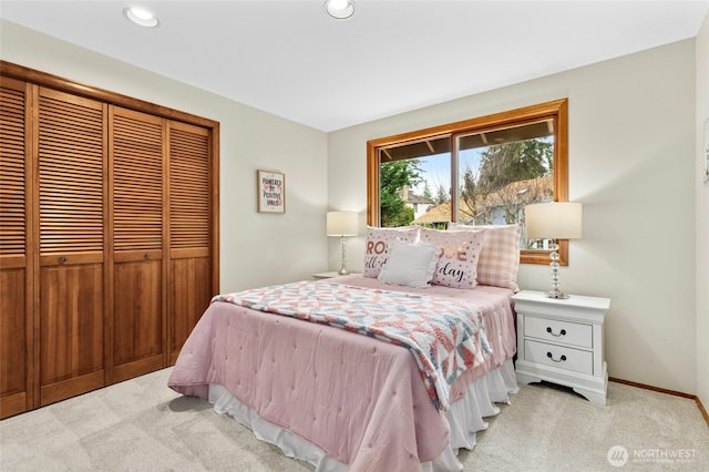 bedroom with a closet, recessed lighting, light colored carpet, and baseboards