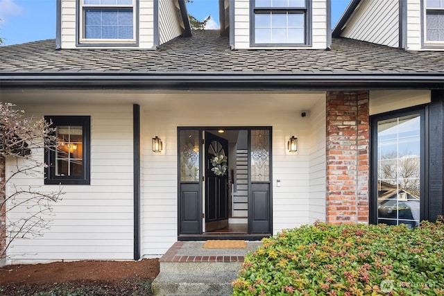 property entrance featuring a shingled roof, brick siding, and a porch