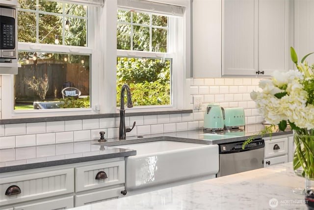 kitchen with tasteful backsplash, dark stone countertops, stainless steel appliances, white cabinetry, and a sink