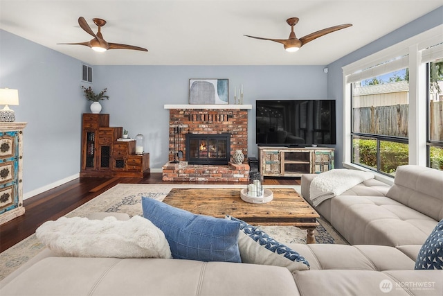 living room with a fireplace, visible vents, a ceiling fan, wood finished floors, and baseboards