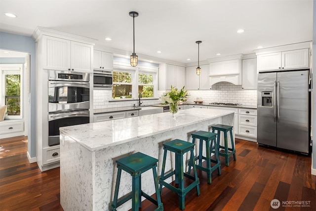 kitchen featuring dark wood-style flooring, stainless steel appliances, white cabinets, a sink, and light stone countertops