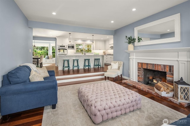 living room with recessed lighting, a brick fireplace, baseboards, and wood finished floors