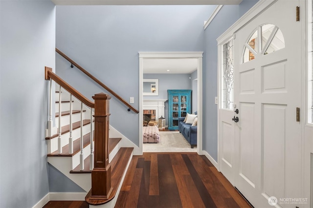 entrance foyer with dark wood-type flooring, a fireplace, baseboards, and stairs