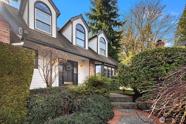 new england style home featuring a shingled roof and brick siding