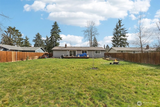 rear view of house featuring a fenced backyard, a fire pit, a deck, and a lawn