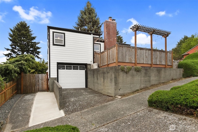 exterior space with a chimney, concrete driveway, a garage, and fence