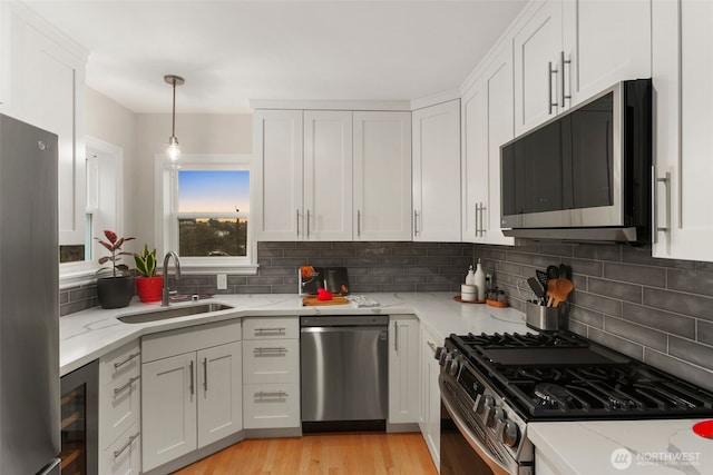 kitchen featuring beverage cooler, a sink, appliances with stainless steel finishes, white cabinets, and light stone countertops