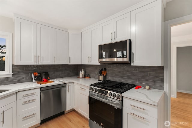 kitchen with light stone counters, white cabinets, stainless steel appliances, and light wood-style floors