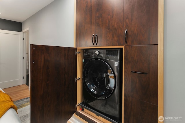 clothes washing area with cabinet space, washer / dryer, and wood finished floors