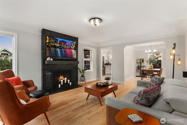 living room featuring arched walkways, a fireplace, crown molding, and light wood-style floors