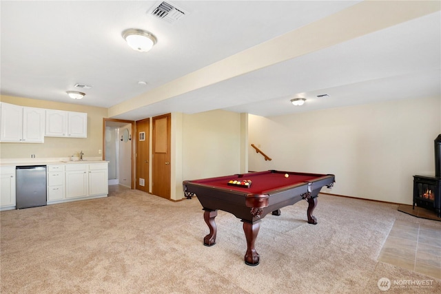 rec room with light carpet, visible vents, indoor wet bar, a wood stove, and a sink