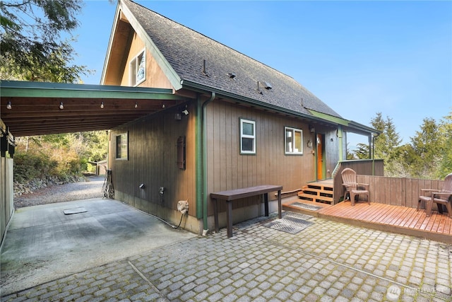 rear view of house with a shingled roof, a patio, a carport, and a wooden deck