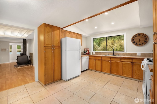 kitchen featuring white appliances, a sink, vaulted ceiling, brown cabinets, and a wood stove