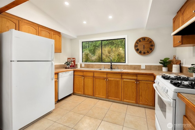 kitchen featuring light tile patterned floors, white appliances, brown cabinetry, and a sink