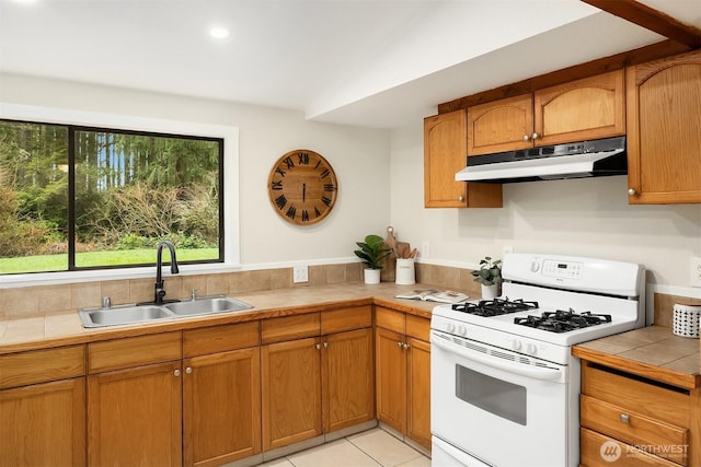 kitchen featuring light tile patterned flooring, under cabinet range hood, a sink, white gas range oven, and tile counters