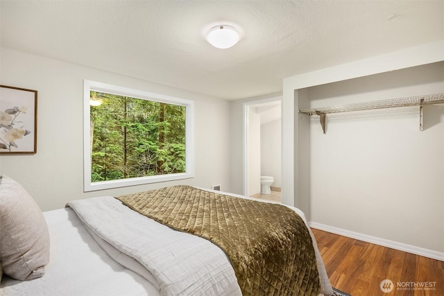 bedroom featuring connected bathroom, a textured ceiling, baseboards, and wood finished floors