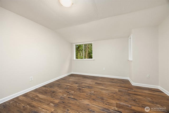 unfurnished room with vaulted ceiling, dark wood-style flooring, a textured ceiling, and baseboards