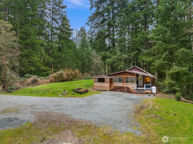 view of front of property with gravel driveway, a front lawn, and a view of trees