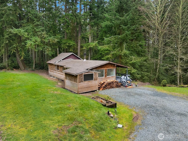 view of front of home featuring a shingled roof, a front yard, gravel driveway, and a view of trees