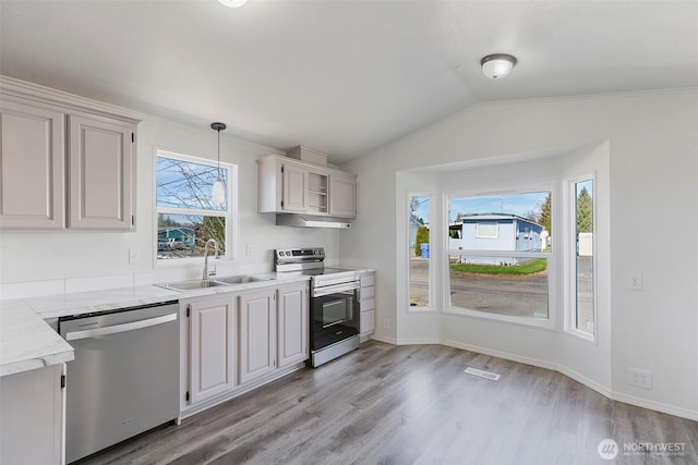 kitchen featuring lofted ceiling, a sink, light wood-style floors, appliances with stainless steel finishes, and baseboards