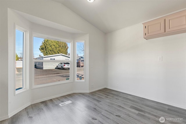 unfurnished dining area featuring vaulted ceiling, light wood-style floors, visible vents, and baseboards