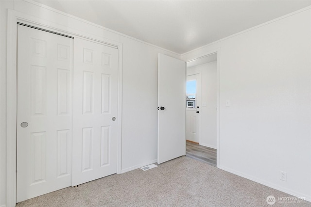 unfurnished bedroom featuring visible vents, a closet, carpet, crown molding, and baseboards