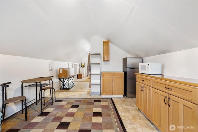 kitchen featuring white microwave, freestanding refrigerator, vaulted ceiling, light countertops, and light brown cabinets