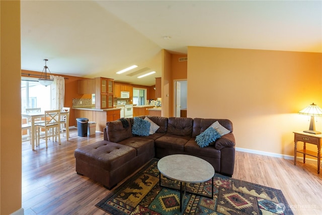 living area with light wood-type flooring, baseboards, visible vents, and vaulted ceiling