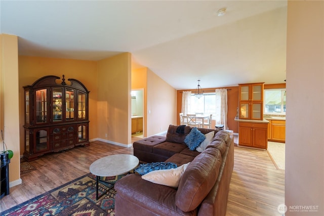 living area with vaulted ceiling, light wood finished floors, and baseboards