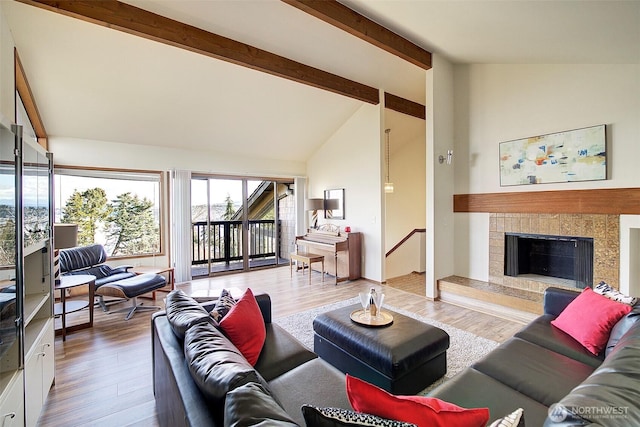 living area featuring beam ceiling, high vaulted ceiling, a fireplace with raised hearth, and wood finished floors