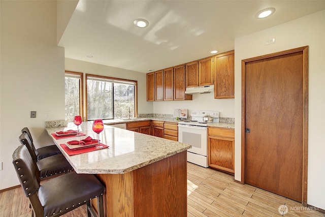 kitchen featuring a breakfast bar, white electric range, light wood-style flooring, a peninsula, and under cabinet range hood