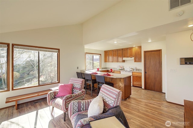 kitchen with white electric stove, under cabinet range hood, visible vents, vaulted ceiling, and brown cabinets