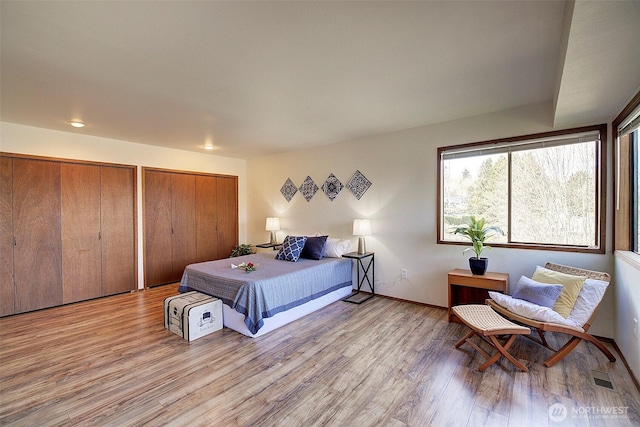 bedroom featuring two closets, baseboards, visible vents, and wood finished floors