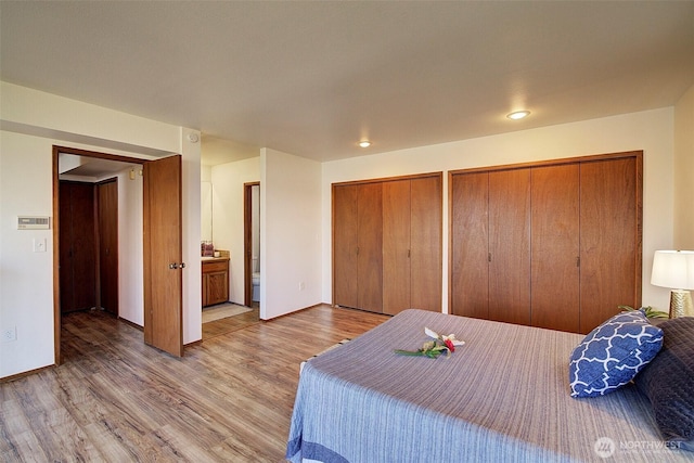 bedroom featuring connected bathroom, baseboards, two closets, and wood finished floors