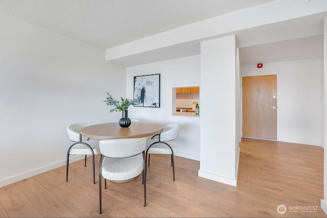 dining room featuring light wood-style floors, a textured ceiling, and baseboards