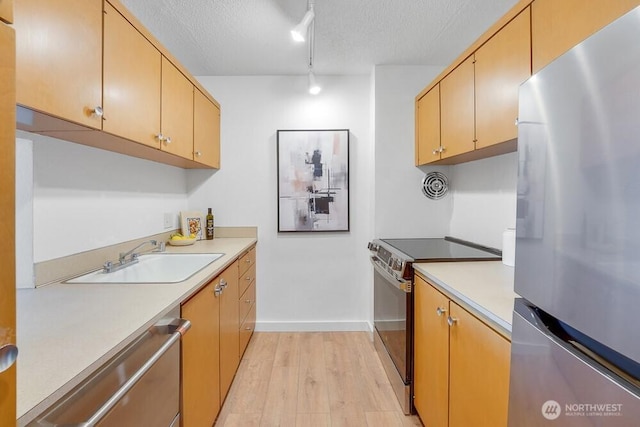 kitchen featuring a textured ceiling, stainless steel appliances, a sink, light wood-style floors, and light countertops