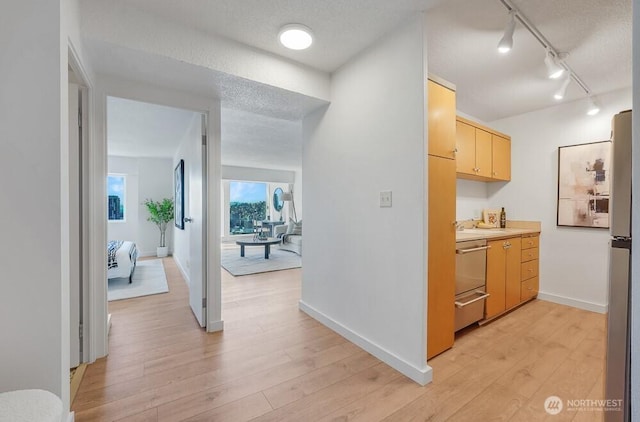 hall featuring a textured ceiling, light wood-style flooring, and baseboards