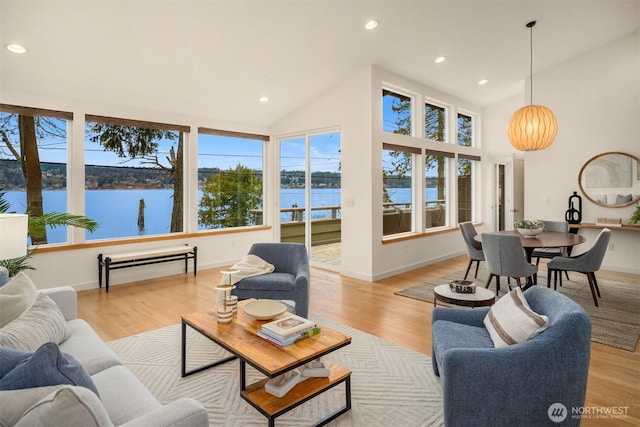 living area with high vaulted ceiling, recessed lighting, a water view, and light wood-style flooring