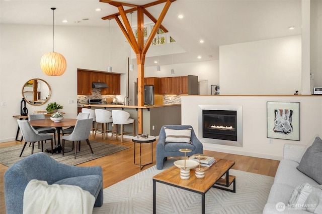 living room with high vaulted ceiling, recessed lighting, a glass covered fireplace, and light wood-style flooring