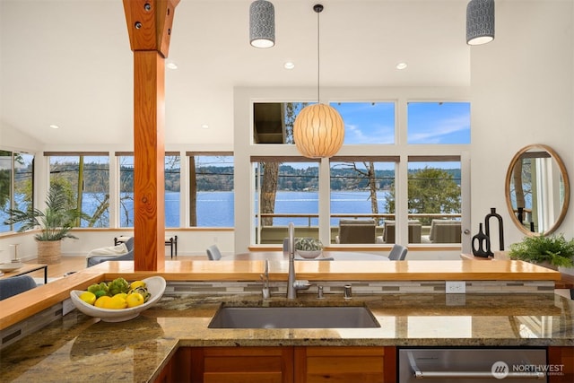 kitchen with stone countertops, a water view, a sink, and stainless steel dishwasher