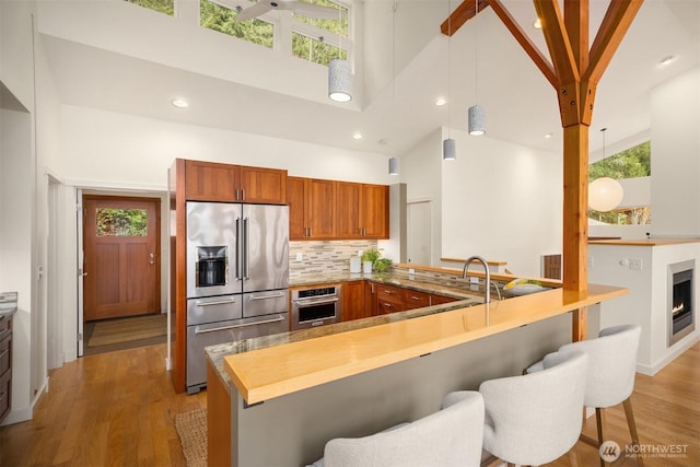 kitchen with a peninsula, appliances with stainless steel finishes, a towering ceiling, and light wood-style floors